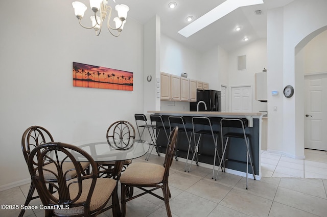 tiled dining room with sink, a skylight, high vaulted ceiling, and a notable chandelier