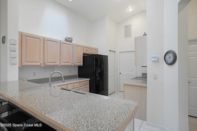 kitchen with light tile patterned flooring, light brown cabinetry, black fridge with ice dispenser, a breakfast bar area, and kitchen peninsula