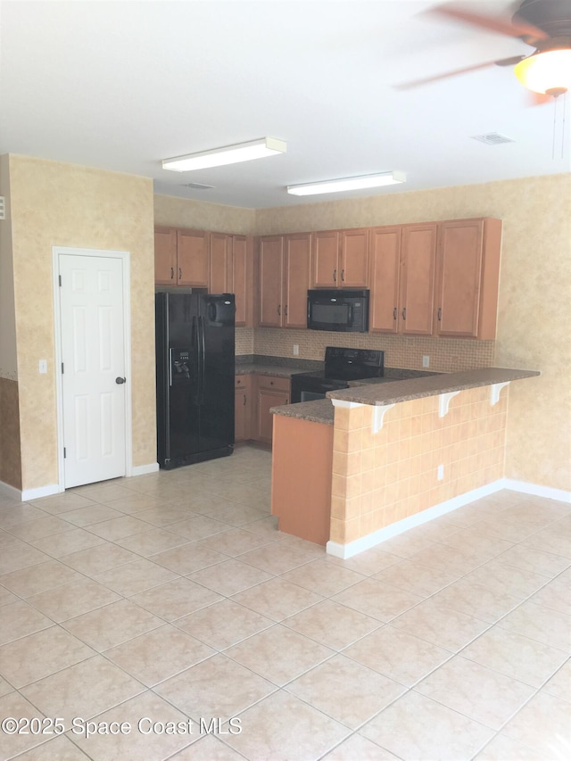 kitchen with light tile patterned floors, a breakfast bar area, backsplash, black appliances, and kitchen peninsula