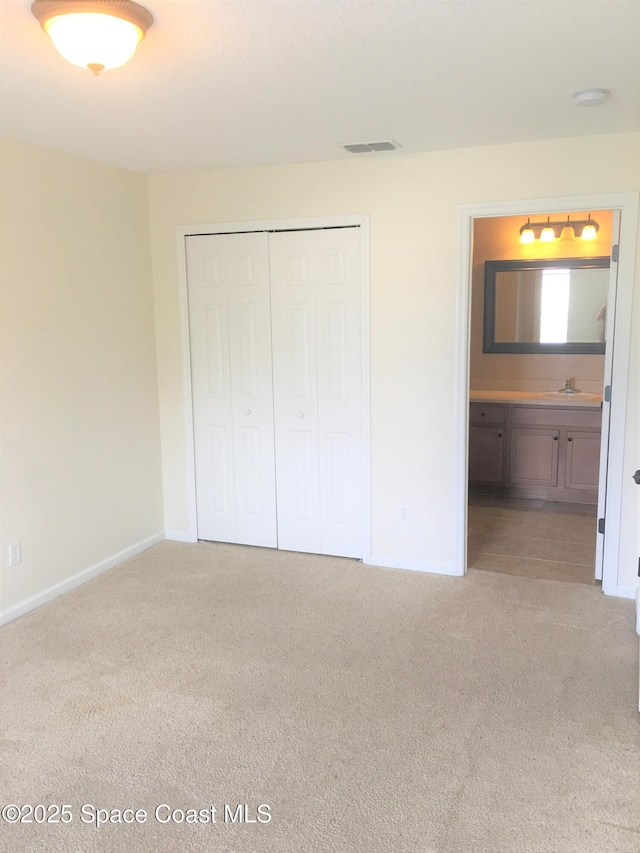 unfurnished bedroom with light colored carpet, ensuite bath, sink, and a closet