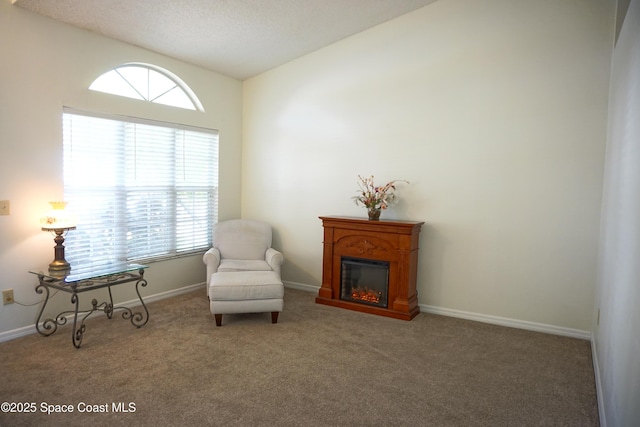 sitting room featuring vaulted ceiling, a glass covered fireplace, a healthy amount of sunlight, and carpet floors