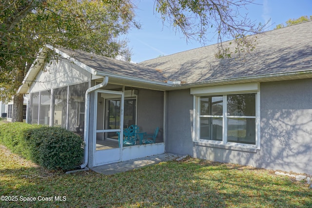 view of home's exterior with a yard, stucco siding, roof with shingles, and a sunroom