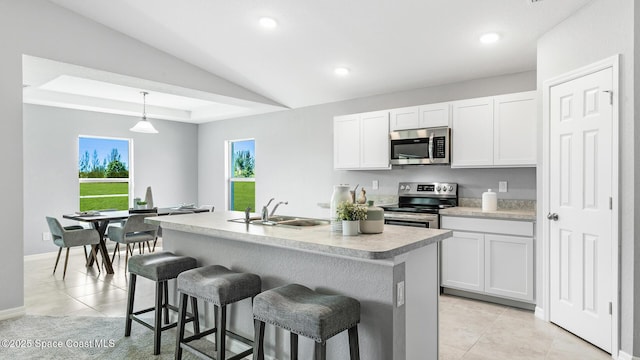 kitchen with sink, a kitchen island with sink, white cabinetry, stainless steel appliances, and decorative light fixtures