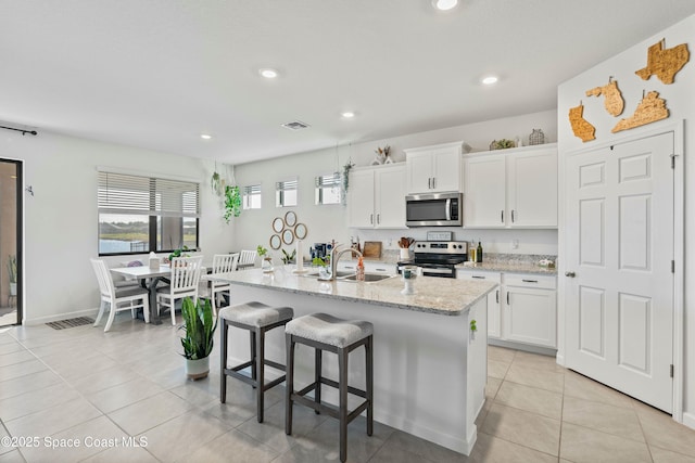 kitchen with sink, white cabinets, a kitchen island with sink, light stone counters, and stainless steel appliances