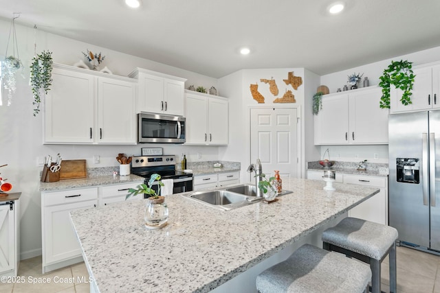 kitchen with stainless steel appliances, white cabinets, and a center island with sink