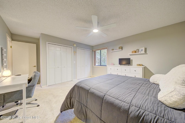 bedroom with light carpet, ceiling fan, two closets, and a textured ceiling