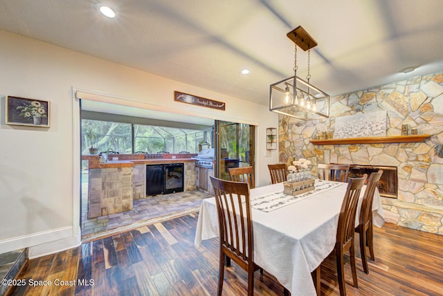 dining room with a stone fireplace, dark wood-type flooring, and beverage cooler