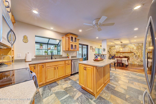 kitchen featuring a kitchen island, sink, hanging light fixtures, ceiling fan, and stainless steel appliances