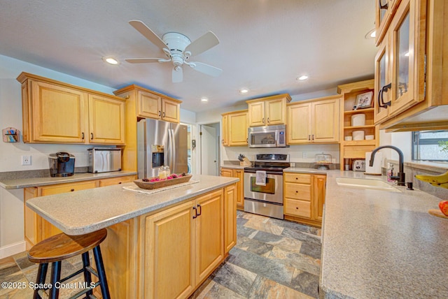 kitchen with a kitchen island, appliances with stainless steel finishes, light brown cabinetry, sink, and a kitchen breakfast bar