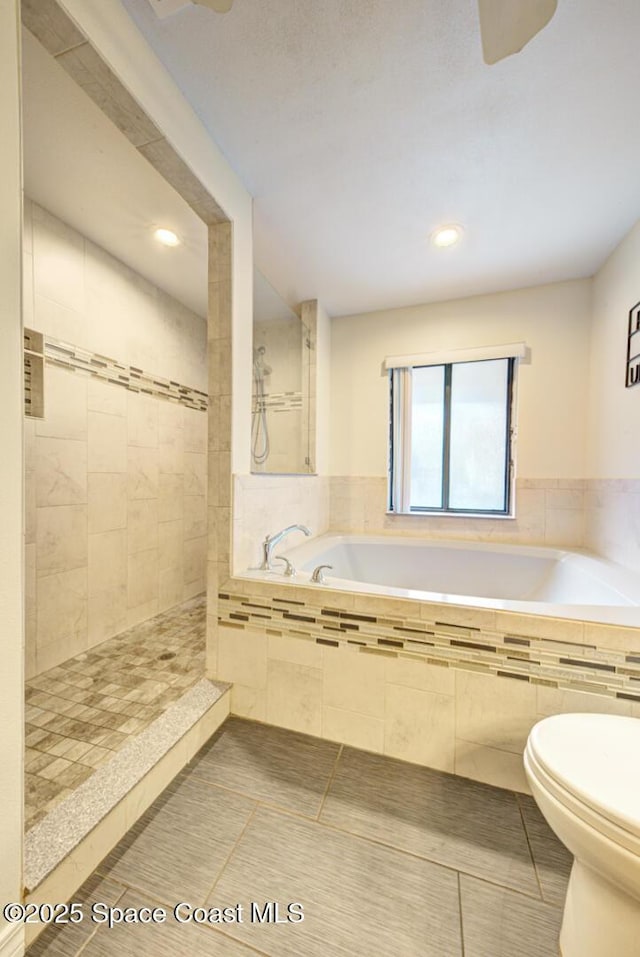 bathroom featuring a relaxing tiled tub, tile patterned floors, and toilet