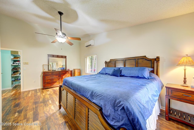 bedroom featuring lofted ceiling, a wall unit AC, dark hardwood / wood-style flooring, a spacious closet, and a textured ceiling