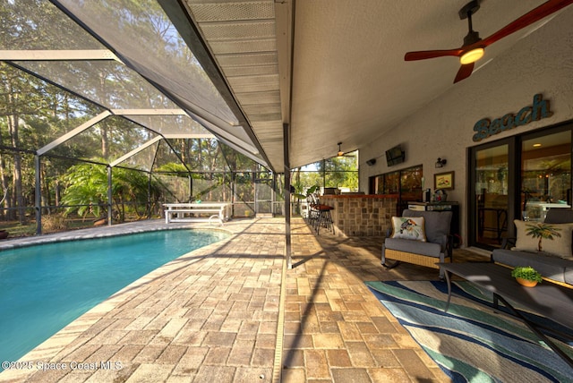 view of swimming pool featuring ceiling fan, exterior bar, glass enclosure, and a patio area