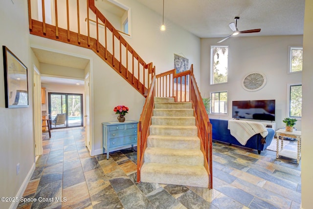 stairs with ceiling fan, a towering ceiling, and a textured ceiling