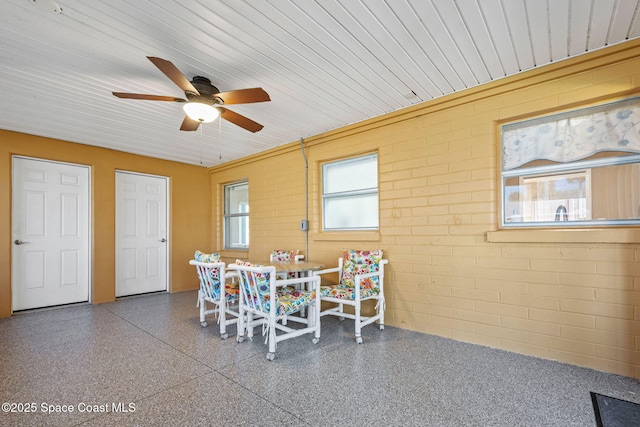 dining space featuring ceiling fan and brick wall