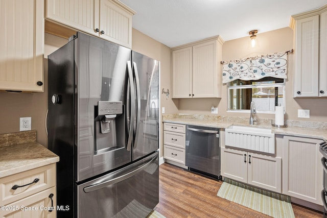 kitchen featuring cream cabinets, stainless steel appliances, sink, and light wood-type flooring