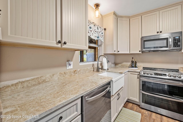 kitchen with sink, light hardwood / wood-style flooring, appliances with stainless steel finishes, light stone counters, and cream cabinetry