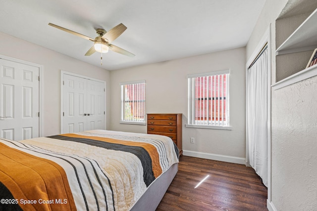 bedroom with dark wood-type flooring, ceiling fan, and two closets