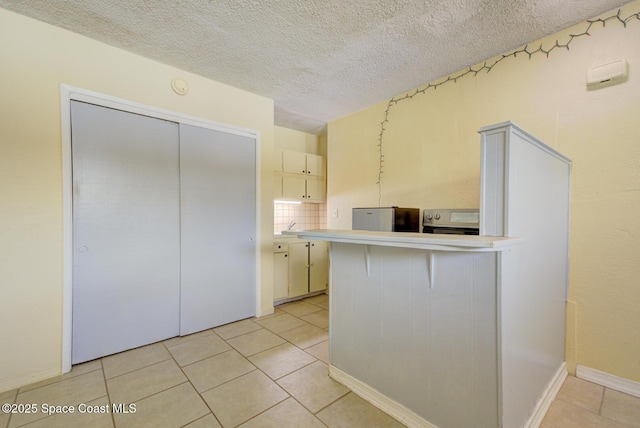 kitchen featuring light tile patterned flooring, decorative backsplash, kitchen peninsula, a textured ceiling, and electric stove