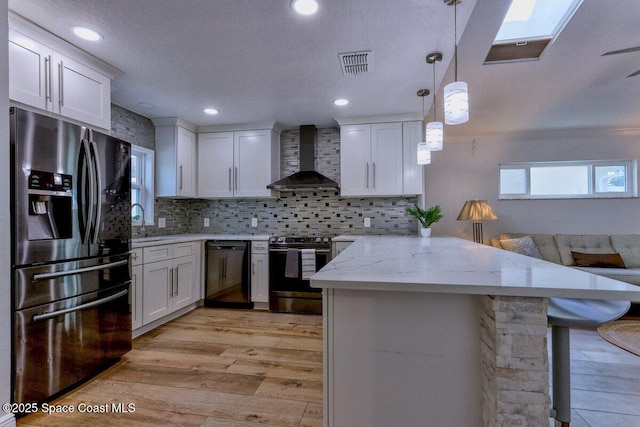 kitchen with wall chimney range hood, hanging light fixtures, white cabinets, and appliances with stainless steel finishes