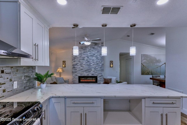 kitchen with a stone fireplace, white cabinetry, backsplash, light stone counters, and wall chimney exhaust hood