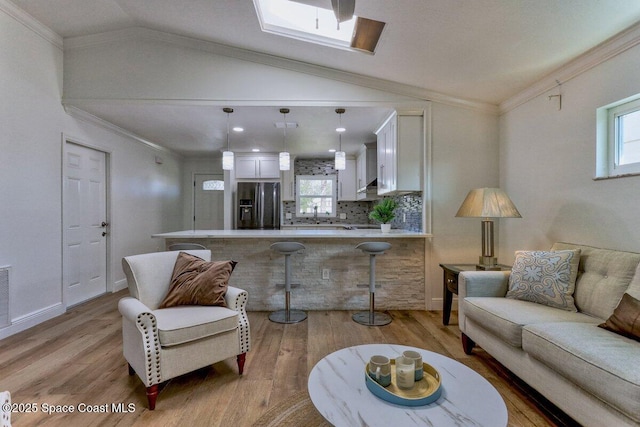 living room featuring ornamental molding, light hardwood / wood-style floors, and vaulted ceiling