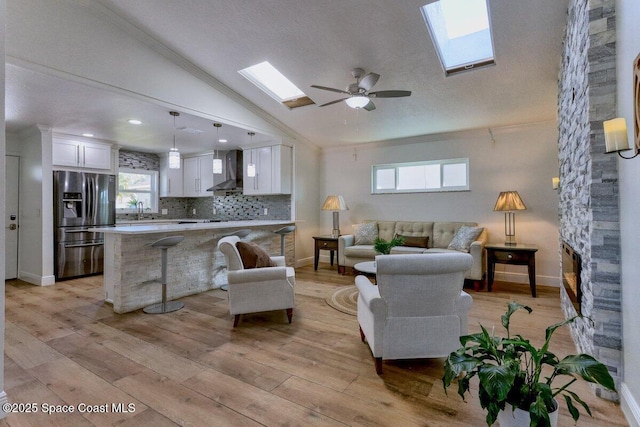 living room featuring lofted ceiling with skylight, sink, light hardwood / wood-style flooring, ceiling fan, and a fireplace