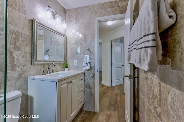 bathroom featuring hardwood / wood-style flooring, tile walls, vanity, ornamental molding, and toilet