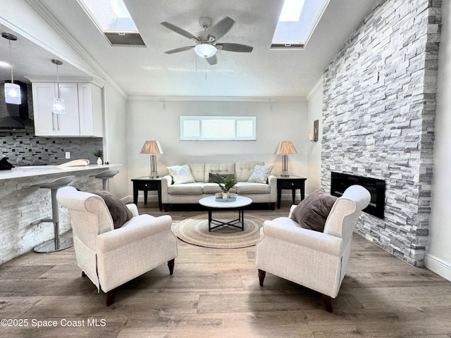 living room featuring dark wood-type flooring, crown molding, a skylight, and a stone fireplace