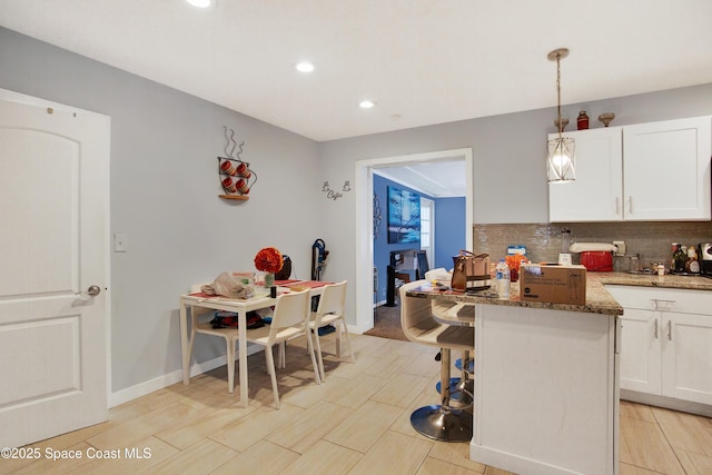 kitchen with tasteful backsplash, white cabinets, a kitchen breakfast bar, dark stone counters, and hanging light fixtures