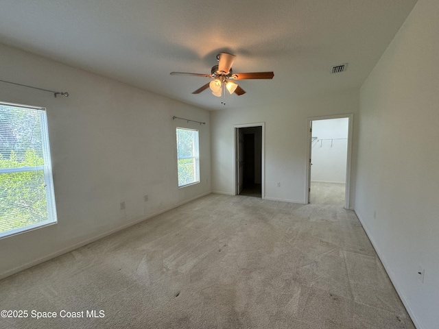 unfurnished bedroom with a walk in closet, light carpet, a textured ceiling, and ceiling fan