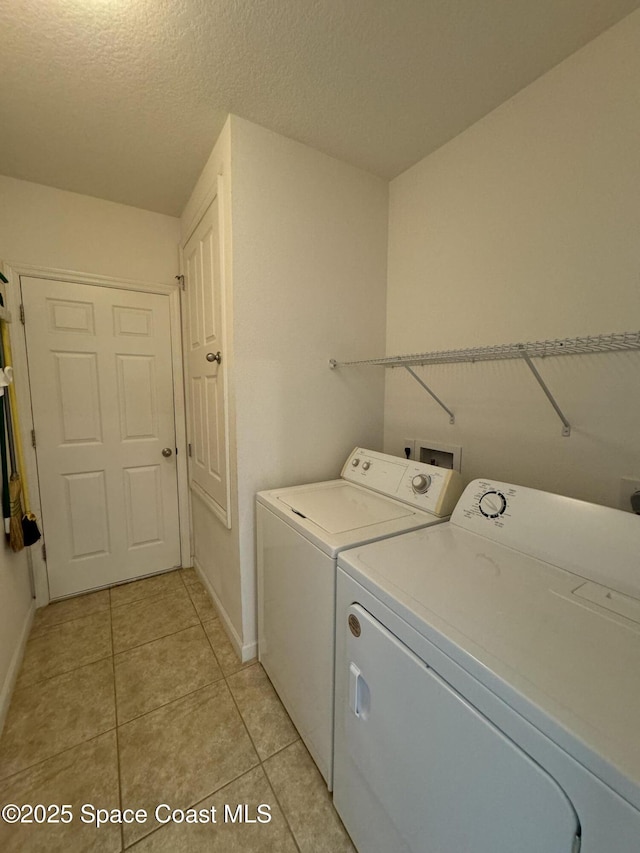 clothes washing area featuring light tile patterned flooring, independent washer and dryer, and a textured ceiling