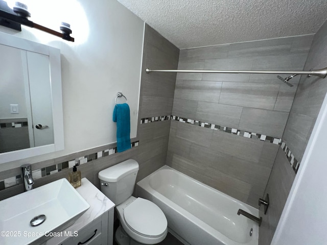 full bathroom with tile walls, vanity, a textured ceiling, tiled shower / bath, and toilet