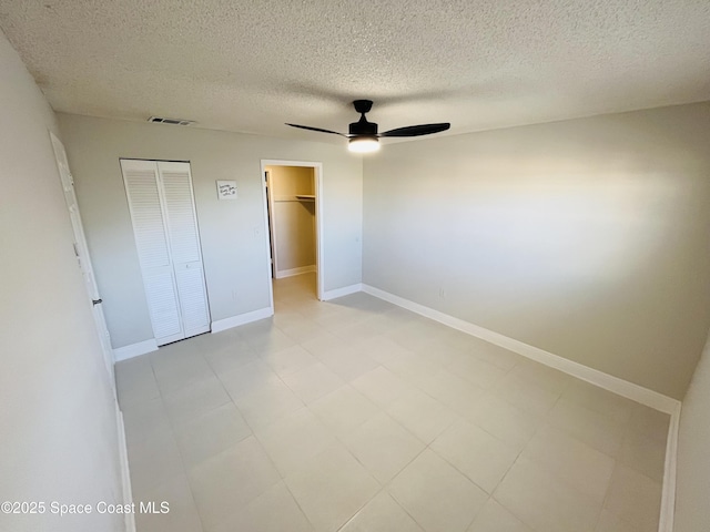 unfurnished bedroom with ceiling fan, a walk in closet, a closet, and a textured ceiling