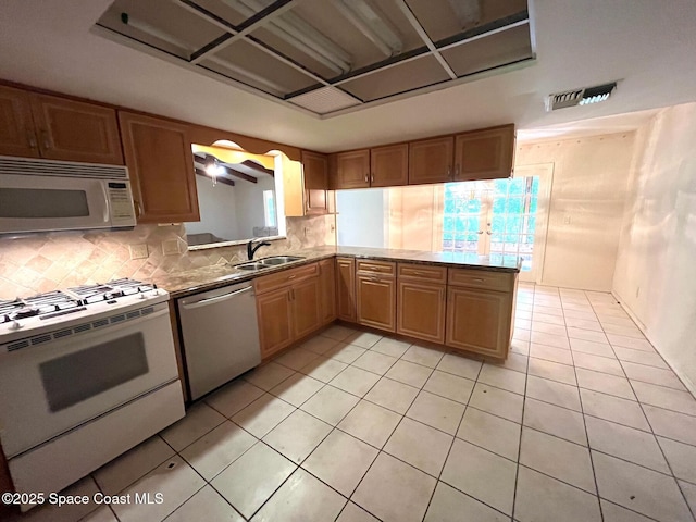 kitchen featuring sink, light tile patterned floors, kitchen peninsula, white appliances, and decorative backsplash