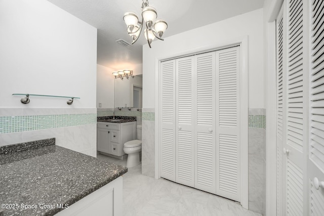 bathroom with vanity, toilet, tile walls, and an inviting chandelier