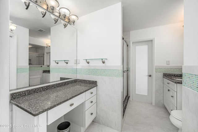 bathroom with walk in shower, vanity, toilet, and tile walls