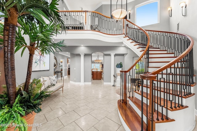 tiled foyer with ornate columns, ornamental molding, and a high ceiling