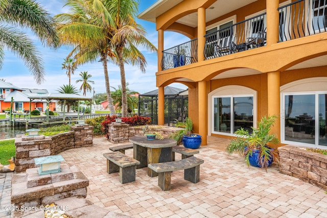 view of patio featuring a lanai, a balcony, and a water view