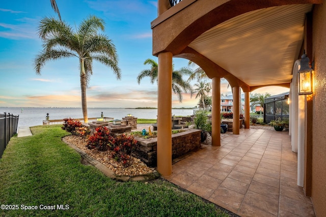 patio terrace at dusk featuring a lawn and a water view