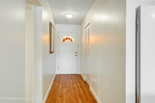 corridor featuring baseboards, light wood-style floors, and a textured ceiling
