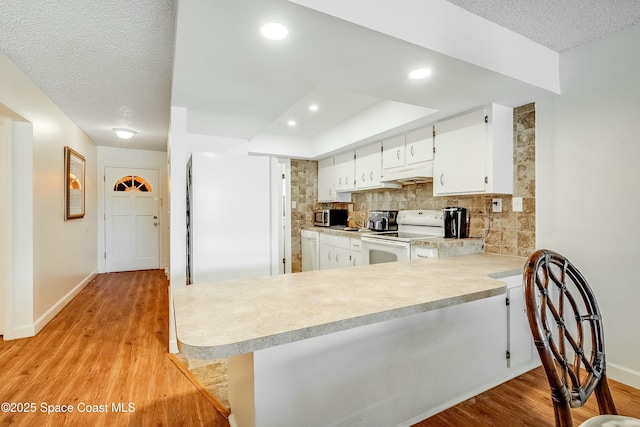 kitchen featuring light countertops, tasteful backsplash, light wood-style floors, and white appliances