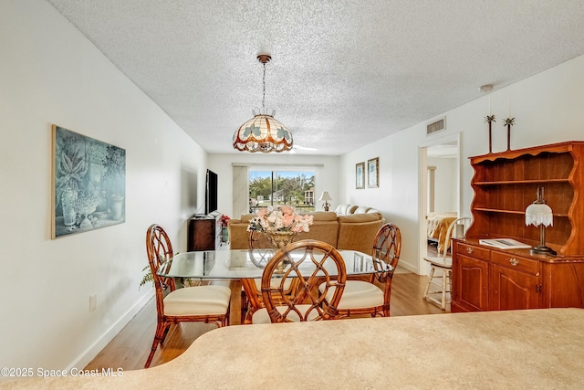 dining area with baseboards, visible vents, light wood-style floors, and a textured ceiling