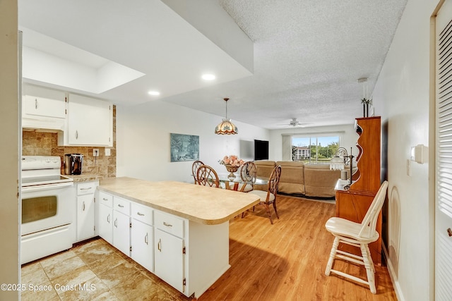 kitchen featuring decorative backsplash, light countertops, range hood, a peninsula, and electric stove
