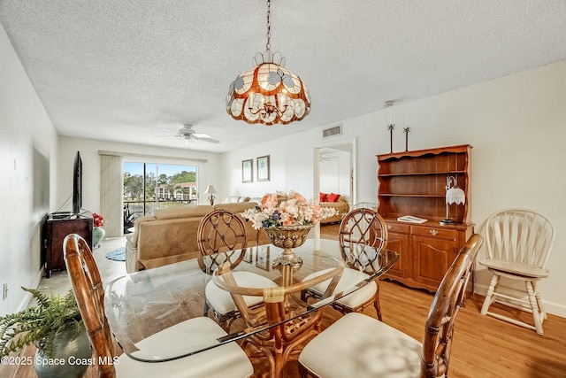dining room with a textured ceiling, baseboards, visible vents, light wood-style floors, and ceiling fan