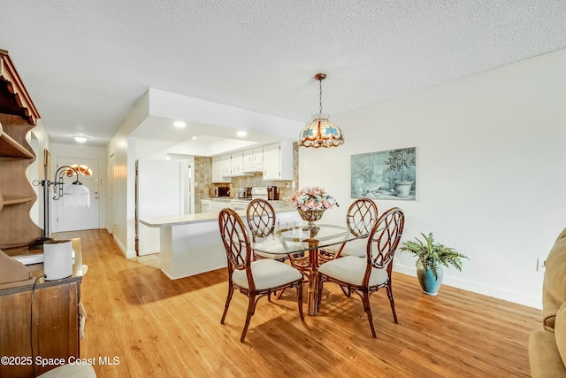 dining area featuring light wood-style flooring, baseboards, a chandelier, and a textured ceiling