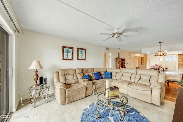 living room featuring ceiling fan with notable chandelier, a textured ceiling, and visible vents