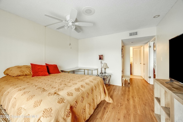 bedroom with a textured ceiling, visible vents, ceiling fan, and light wood-type flooring