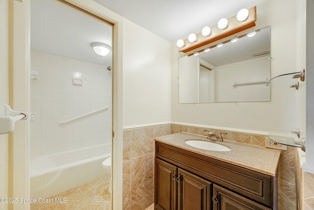 full bathroom with tile walls, toilet, vanity, tile patterned flooring, and wainscoting