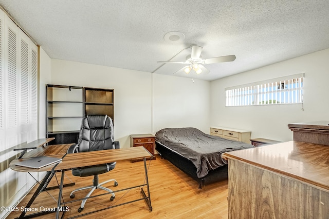 bedroom with a textured ceiling, light wood-style floors, and a ceiling fan