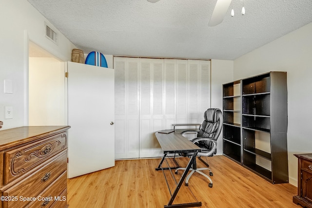home office featuring a textured ceiling, visible vents, a ceiling fan, and light wood finished floors